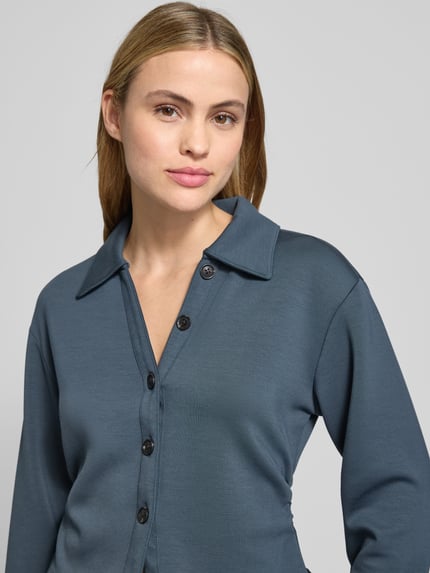 Frauenmodel trägt Cropped Blusenshirt mit Umlegekragen und Knopfleiste von Scotch & Soda in blauem Material-Mix mit Micromodal-Anteil, Nahaufnahme Oberkörper.