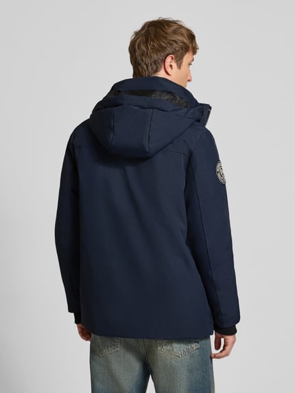 Männermodel trägt granatową parkę z kapturem i kieszeniami z patką, materiał gładki, Parka mit Kapuze und Pattentaschen von Superdry, krój regular fit, zakryty zamek błyskawiczny, Długość tyłu w rozmiarze M: 80 cm, szerokość ramion w rozmiarze M: 48 cm, szerokość klatki piersiowej w rozmiarze M: 61 cm, Długość rękawów w rozmiarze M: 73 cm, Ganzkörperansicht Rückansicht.