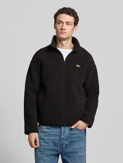 Männermodel trägt Bomberjacke mit Logo-Detail von LACOSTE, unifarbenes Design, Stehkragen, elastische Abschlüsse, Reißverschluss, Nahaufnahme Oberkörper.