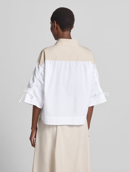 Frauenmodel trägt Boxy Fit Bluse mit 3/4-Arm von Marc Cain aus reiner Baumwolle, Hemdblusenkragen, Knopfleiste, zweifarbig, Ganzkörperansicht Rückansicht.