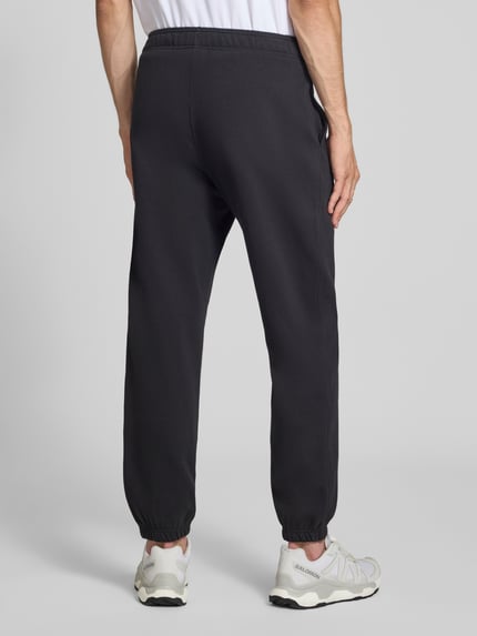 Männermodel trägt zwarte sweatpants met labelstitching Model 'ICONS' van Champion, katoenmix, recht model, elastische band, steekzakken, binnenbeenlengte maat M 76 cm, ganzkörperansicht rückansicht.