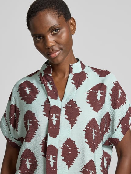 Kobiece modelka nosi Bluse aus Viskose-Mix mit Ärmelaufschlag von Christian Berg Woman, wzór w brązowe i miętowe kształty, tunikowy kołnierz, zakładka na rękawach, mieszanka wiskozy, krój straight fit, długość tyłu 69 cm w rozmiarze 36, zbliżenie na górną część ciała