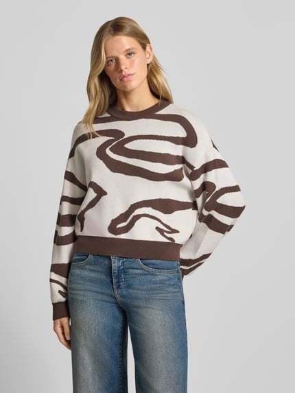 Modelka kobieca nosi Relaxed Fit Pullover aus Viskose-Mix Modell 'Charlott' od NOISY MAY®, wzór animal-print, kolory beżowy i brązowy, długie rękawy, okrągły dekolt, ściągacze, widoczna miękka tekstura, Ganzkörperansicht von vorne.