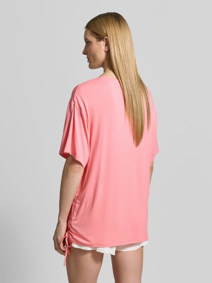 Modelka nosi damski t-shirt z mieszanki wiskozy, luźny krój, nadruk z logo, tunel, model 'COULISSE' od Guess, widok z tyłu całej sylwetki.