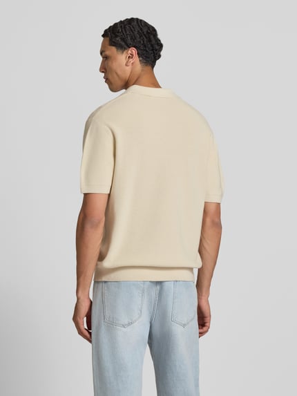 Männermodel trägt Boxy Fit Poloshirt mit Logo-Stitching van REVIEW in beige, puur katoen, polokraag, korte ritssluiting, ruglengte maat M 67 cm, ganzlichaamsaanzicht achteraan.
