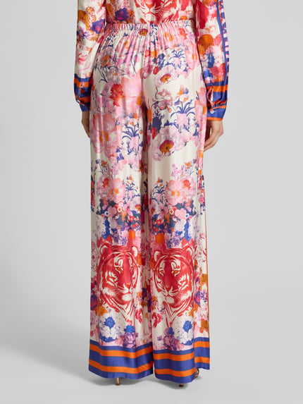 Frauenmodel trägt Wide Leg Hose aus Viskose Modell 'wild Flower' von miss goodlife, bunter Blumen- und Tigerprint, glänzende Textur, Ganzkörperansicht Rückansicht. Damenhose mit Knopfverschluss, Teilungsnähten, Bundweite 35 cm, Innenbeinlänge 88 cm bei Größe S.