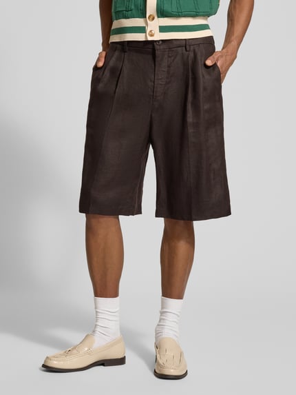 Mannenmodel draagt Leinenshorts aus reinen Leinen van Drykorn in donkerbruin, los vallende fit, met steek- en achterzakken, knoop- en ritssluiting, kelderplooien, pure linnenstructuur, voorkant compleet zicht, modieuze context.