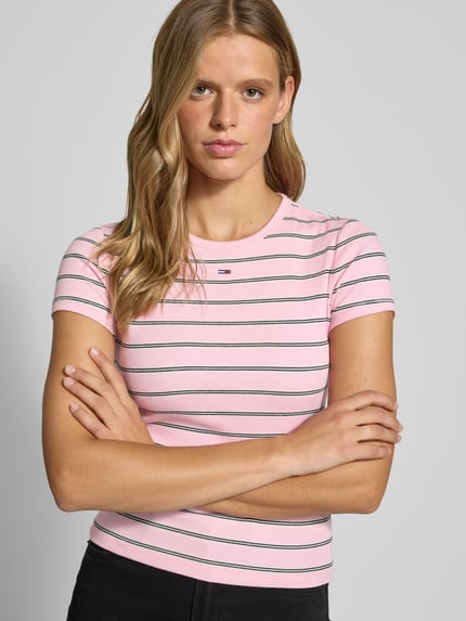 Frauenmodel trägt Slim Fit T-Shirt aus Baumwoll-Mix von Tommy Jeans, rosa mit weißen und schwarzen Streifen, Nahaufnahme Oberkörper. Damen T-Shirt von Tommy Jeans.