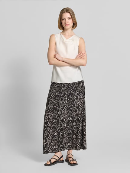 Frauenmodel trägt Ausgestellter Maxi-Rock aus reiner Viskose Modell 'EASY JOY' von Vero Moda mit grafischem Allover-Muster in Schwarz und Weiß, Popeline-Struktur, elastischer Bund, Ganzkörperansicht von vorne.