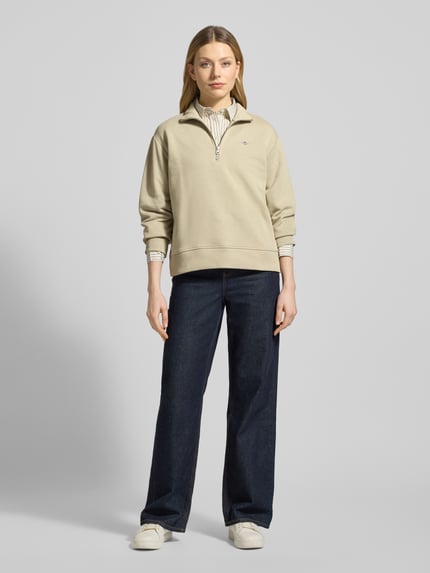 Frauenmodel trägt Sweatshirt mit Baumwoll-Anteil von Gant in Beige, lockerer Schnitt, Troyer-Kragen, Label-Stitching, gerippte Abschlüsse, Ganzkörperansicht von vorne.