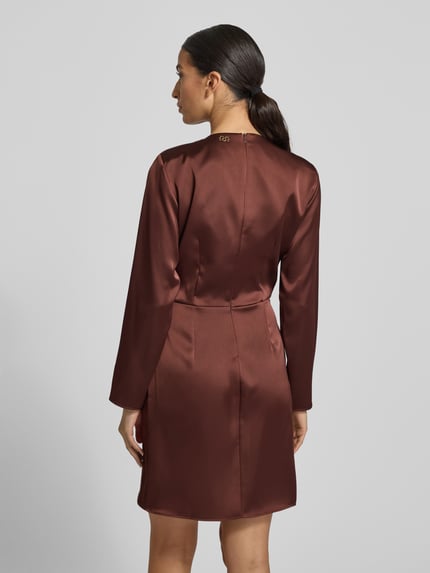 Frauenmodel trägt knielanges Cocktailkleid mit Rundhalsausschnitt von Rinascimento aus braunem Satin, körpernahe Passform, asymmetrischer Saum, Rückenlänge 91 cm, Brustweite 47 cm, Ärmellänge 59 cm, Ganzkörperansicht Rückansicht.