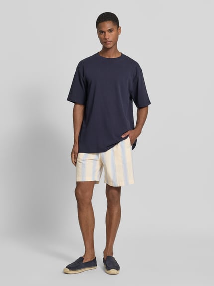 Männermodel trägt Regular Fit Shorts aus reiner Baumwolle von Armedangels, Optik:Allover-Muster, gestreift, Twill, Ganzkörperansicht von vorne.
