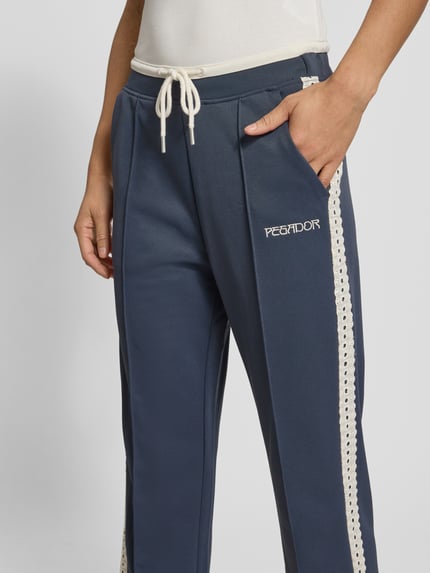 Frauenmodel trägt Trackpants mit Spitzenbesatz Modell 'TIHANY LACE' von Pegador, Blau mit cremefarbenen Details, Material-Mix mit Baumwoll-Anteil, Regular-Fit, Label-Stitching, Nahaufnahme Oberkörper.