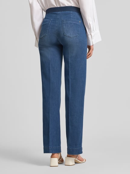 Frauenmodel trägt Damen Wide Leg Jeans mit Eingrifftaschen Modell 'Jenny' von TONI, blaue Baumwoll-Lyocell-Mischung in ausgestelltem Schnitt, mit elastischem Bund, Knopf-, Reißverschluss und Gesäßtaschen, Ganzkörperansicht Rückansicht.
