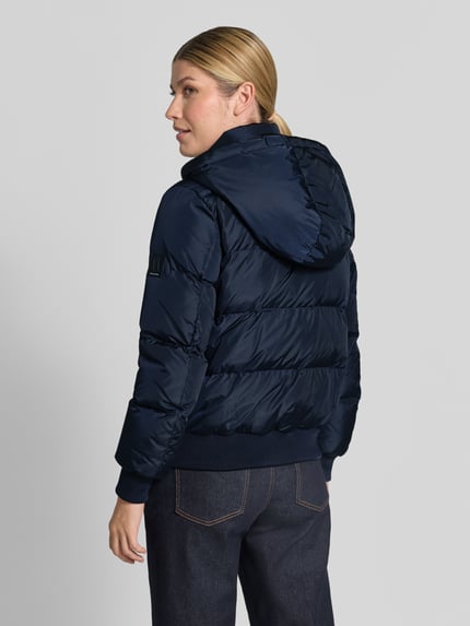 Vrouwenmodel draagt Steppjacke met Daunen-Feder-Füllung van Armani Exchange in donkerblauw met elastische materiaalmix, regular fit, opstaande kraag, tweewegritssluiting, ritszakken en capuchon, ruglengte maat S 60 cm, schouderbreedte 41 cm, borstwijdte 50 cm, mouwlengte 62 cm. Ganzkörperansicht Rückansicht