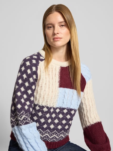 Frauenmodel trägt Pullover mit Ballonärmeln Modell 'VMKRISTIN' von VERO MODA, Patchwork-Strickoptik mit Jacquard, Nahaufnahme Oberkörper.