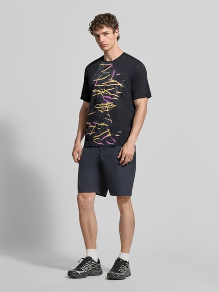 Männermodel trägt Herren T-Shirt mit Logo- und Motiv-Print Modell 'Kout' von Salomon in Dunkelgrau, Gerader-Schnitt, Rundhalsausschnitt, Ganzkörperansicht von vorne. Rückenlänge bei Größe M: 70 cm.