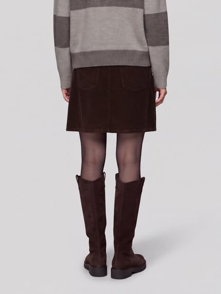 Frauenmodel trägt Rock mit Cordstruktur von S.OLIVER CASUAL in Dunkelbraun, Mini-Länge, strukturierte Oberfläche, Rückansicht Ganzkörperansicht.