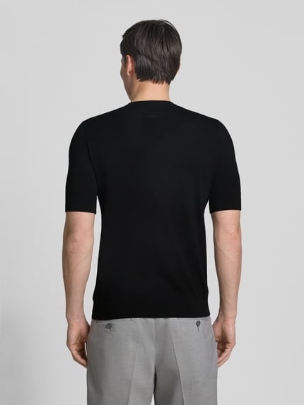 Männermodel trägt Slim Fit T-Shirt aus Strick von HUGO in Schwarz, kurzarm, Rundhals, Label Stitching, Ganzkörperansicht Rückansicht.