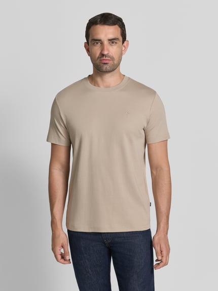 Męski model nosi T-Shirt mit Rundhalsausschnitt und Logo-Stitching von JOOP! aus bawełny, krój regular fit, okrągły dekolt, beżowy, wyhaftowane logo, kolekcja, Długość tyłu w rozmiarze M: 68 cm, widok całej sylwetki z przodu.