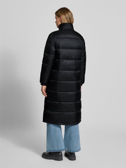 Frauenmodel trägt Regular Fit Steppmantel mit verdeckter Kapuze von Tommy Jeans, unifarben schwarz, Longline, Rückansicht, Ganzkörperansicht.