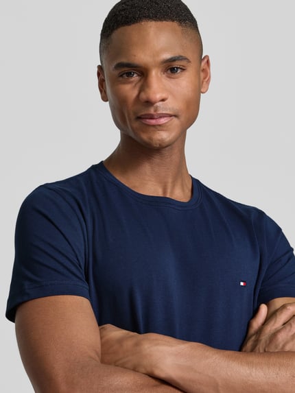 Männermodel trägt Slim Fit T-Shirt aus Baumwoll-Mix von Tommy Hilfiger in effen donkerblauw met logo-detail, stretchmateriaal, nahaufnahme oberkörper.