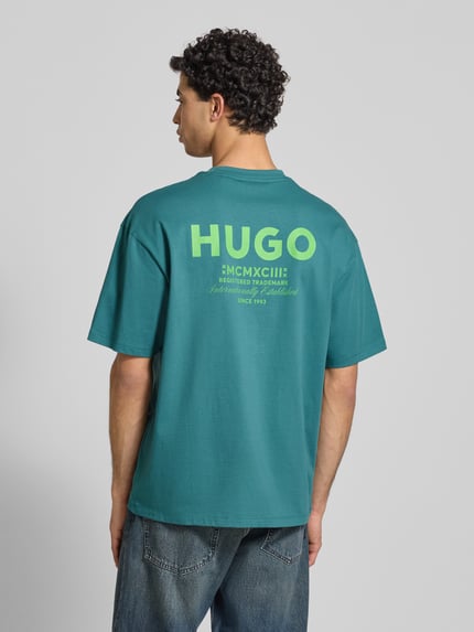 Männermodel trägt Oversized T-Shirt aus reiner Baumwolle Modell 'NALONO' von Hugo Blue in Unifarbe mit Label Print, Ganzkörperansicht Rückansicht.