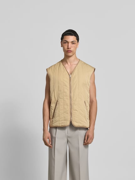 Męski model nosi Relaxed Fit Weste in Stepp-Optik od MM6 Maison Margiela, beżowa, z kieszeniami, dekoltem V i zamkiem, długość tyłu 70 cm, szerokość w rozmiarze 50: 61 cm, ganzkörperansicht von vorne.