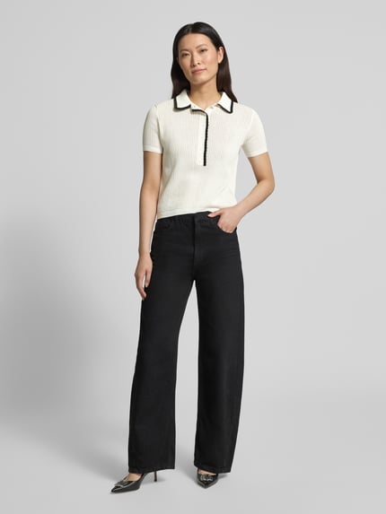Modelka nosi Regular Fit Strick-Shirt aus reiner Baumwolle Modell 'SLYSA' od HUGO, białe, prążkowana struktura, logo, kontrastowe lamówki, krótkie rękawy, dzianina, bawełna. Ganzkörperansicht von vorne.