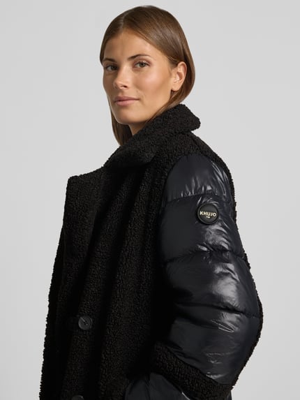 Frauenmodel trägt Steppmantel mit doppelreihiger Knopfleiste Modell 'KALMIA' von khujo, schwarze Farbe, Woll-Optik, Nahaufnahme Oberkörper.