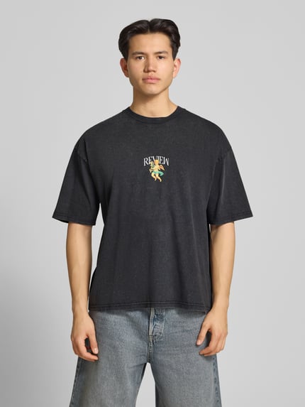 Männermodel trägt T-Shirt mit überschnittenen Schultern von REVIEW, reine Baumwolle, lockerer Schnitt, dunkle Farbe, Ganzkörperansicht von vorne