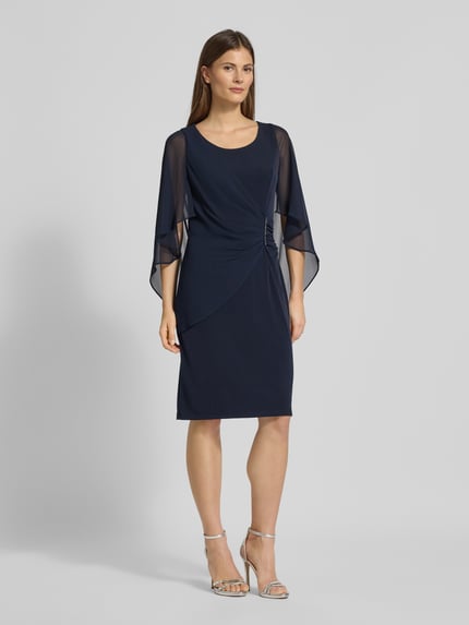 Kobiece modelka nosi Knielanges Cocktailkleid mit Rundhalsausschnitt od Vera Mont, elastyczna mieszanka materiałów, dopasowany krój, okrągły dekolt, kopertowy styl, ozdobna aplikacja z obszyciem z kamieni stras, długość do kolan, wszyty zamek błyskawiczny z tyłu, rękawy nietoperzowe z szyfonu, długość tyłu w rozmiarze 36: 98 cm, szerokość w rozmiarze 36: 108 cm, długość rękawów w rozmiarze 36: 48 cm, granatowy kolor, gładka tekstura, widok całej sylwetki z przodu