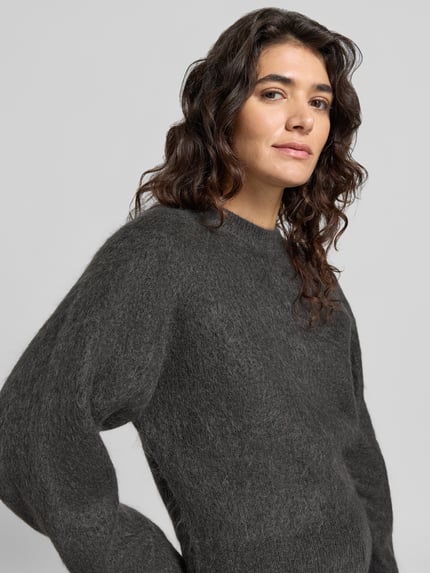 Frauenmodel trägt Pullover aus Mohair mit überschnittenen Schultern von Selected in dunklem Grau, weiche Textur, Nahaufnahme Oberkörper.