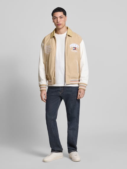 Männermodel trägt Relaxed Fit College-Jacke aus echtem Leder von Tommy Jeans in Lederoptik, naturweiß-beige, Ganzkörperansicht von vorne.