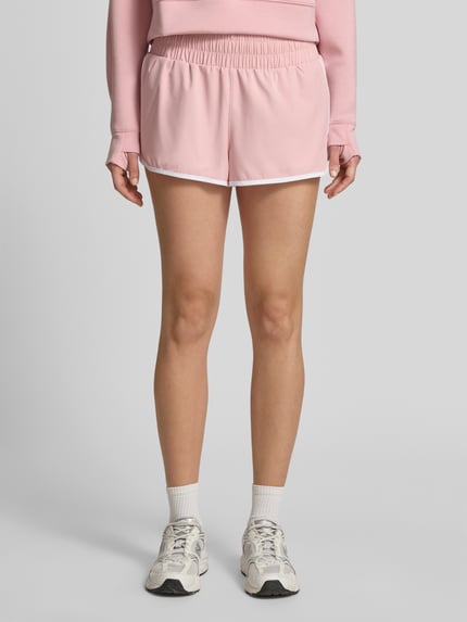 Frauenmodel trägt Running Shorts mit elastischem Bund von VARLEY in Rosa mit weißem Rand, entspannter Schnitt, Material-Mix mit Stretch, Ganzkörperansicht von vorne.