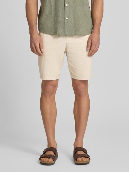 Męski model nosi Regular Fit Shorts aus Baumwoll-Leinen-Mix Modell 'LINUS' von Only & Sons, efekt: jednolity kolor, krój regular fit, aplikacja z metką, elastyczny ściągacz z tunel, wpuszczane kieszenie, kieszeń z tyłu, materiał: mieszanka bawełny i lnu, jasny beż, faktura lekko strukturalna, Ganzkörperansicht von vorne.