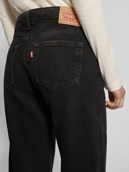 Frauenmodel trägt Superlow Loose Fit Jeans mit Eingrifftaschen von Levi's®, reine Baumwolle, schwarze Denimstruktur, Detailaufnahme Rückansicht.