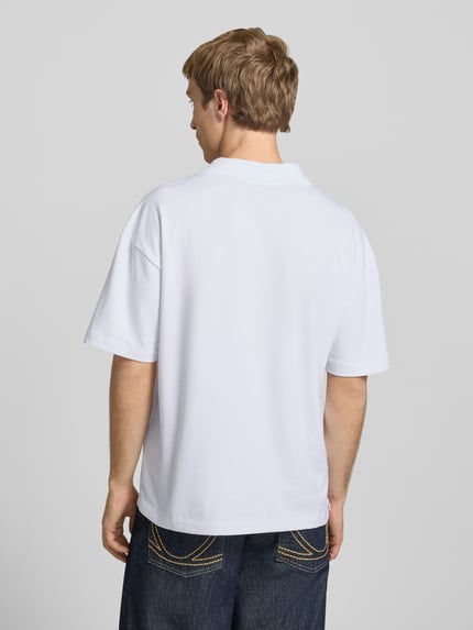 Männermodel trägt Boxy Fit Poloshirt aus Baumwoll-Mix Modell 'CASPIAN AIRLEX' von Only & Sons, weiß, Uni, Label Patch, Ganzkörperansicht Rückansicht.