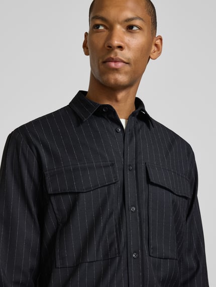 Männermodel trägt Regular Fit Overshirt mit Pattentaschen von Antony Morato, Mieszanka materiałów z dodatkiem wiskozy, krój regular fit, kołnierzyk typu kent, listwa guzikowa, kieszenie z patką, zaokrąglony dół, sportowe mankiety, Długość tyłu w rozmiarze 46: 75 cm, czarne z białymi paskami, tekstura tkaniny, Nahaufnahme Oberkörper.