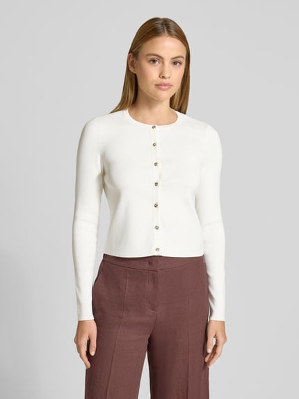 Frauenmodel trägt Slim Fit Cardigan aus Viskose-Mix Modell 'Velda' von Ted Baker, Strick-Optik, langärmelig, Rundhalsausschnitt, Knopfleiste, cremefarben zu brauner Hose, Ganzkörperansicht von vorne.
