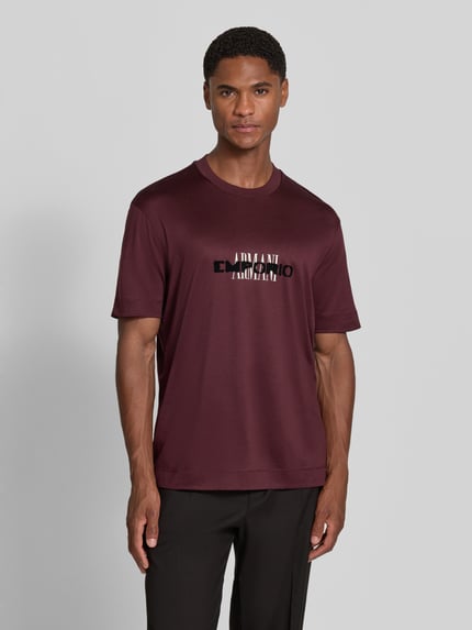 Männermodel trägt T-Shirt mit Label-Print von Emporio Armani in Bordeaux, Lyocell-Baumwoll-Mix, gerader Schnitt, Rundhalsausschnitt, Ganzkörperansicht von vorne.