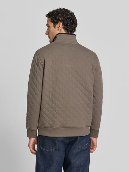 Männermodel trägt Regular Fit Troyer aus Baumwoll-Mix von GANT in Braun mit Stehkragen, Strukturmuster, gerippten Abschlüssen, Ganzkörperansicht Rückansicht.