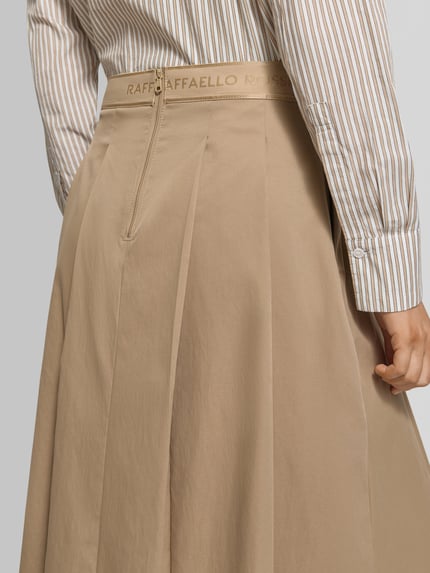 Frauenmodel trägt Midirock mit Nahtreißverschluss Modell 'Vivian' von Raffaello Rossi, Gelegte Falten, Logo-Stitching, Detailaufnahme Rückansicht. Bundweite 38 cm, Gesamtlänge 81 cm bei Größe 36.