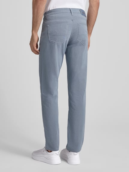Männermodel trägt Slim Fit Stoffhose mit 5-Pocket-Design Modell 'Cadiz' von Brax, hellblaue Farbe, Baumwoll-Mix mit Stretch-Anteil, Ganzkörperansicht Rückansicht.