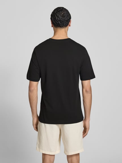 Męski model nosi T-Shirt mit Logo und Rundhalsausschnitt od Jack & Jones, czarny, czysta bawełna, krój regular fit, długość tyłu w rozmiarze M: 71 cm, widok całej sylwetki z tyłu.