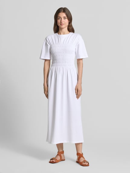 Frauenmodel trägt Midikleid mit Smok-Details von Jake*s Casual in Weiß, reine Baumwolle, taillierter Schnitt, Ganzkörperansicht von vorne.