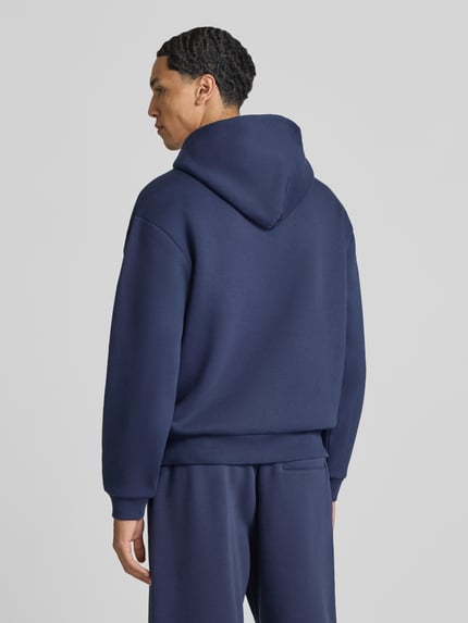 Männermodel trägt Sweatjacke aus Baumwoll-Mix von REVIEW in Dunkelblau, lockere Passform, weiche Textur, Ganzkörperansicht Rückansicht.