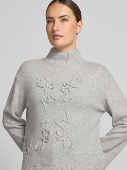 Frauenmodel trägt Strickpullover mit Stehkragen von Christian Berg Woman, hellgrau, gerippte Abschlüsse, lockere Passform, Nahaufnahme Oberkörper.