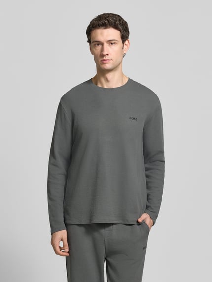 Männermodel trägt Longsleeve mit Logo-Schriftzug von BOSS in Grau, unifarben, Rundhals, langarm, abgerundeter Saum, Nahaufnahme Oberkörper.