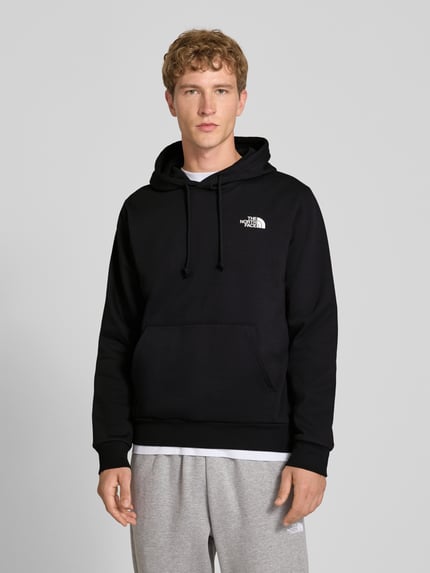 Mannelijk model draagt Regular Fit Hoodie met kap Model "EVOLUTION BOX" van The North Face in zwart katoenmix met kangoeroezak, capuchon met tunnelkoord, elastische boordjes, ruglengte maat M 67 cm, mouwlengte maat M 68 cm, vooraanzicht bovenlichaam.